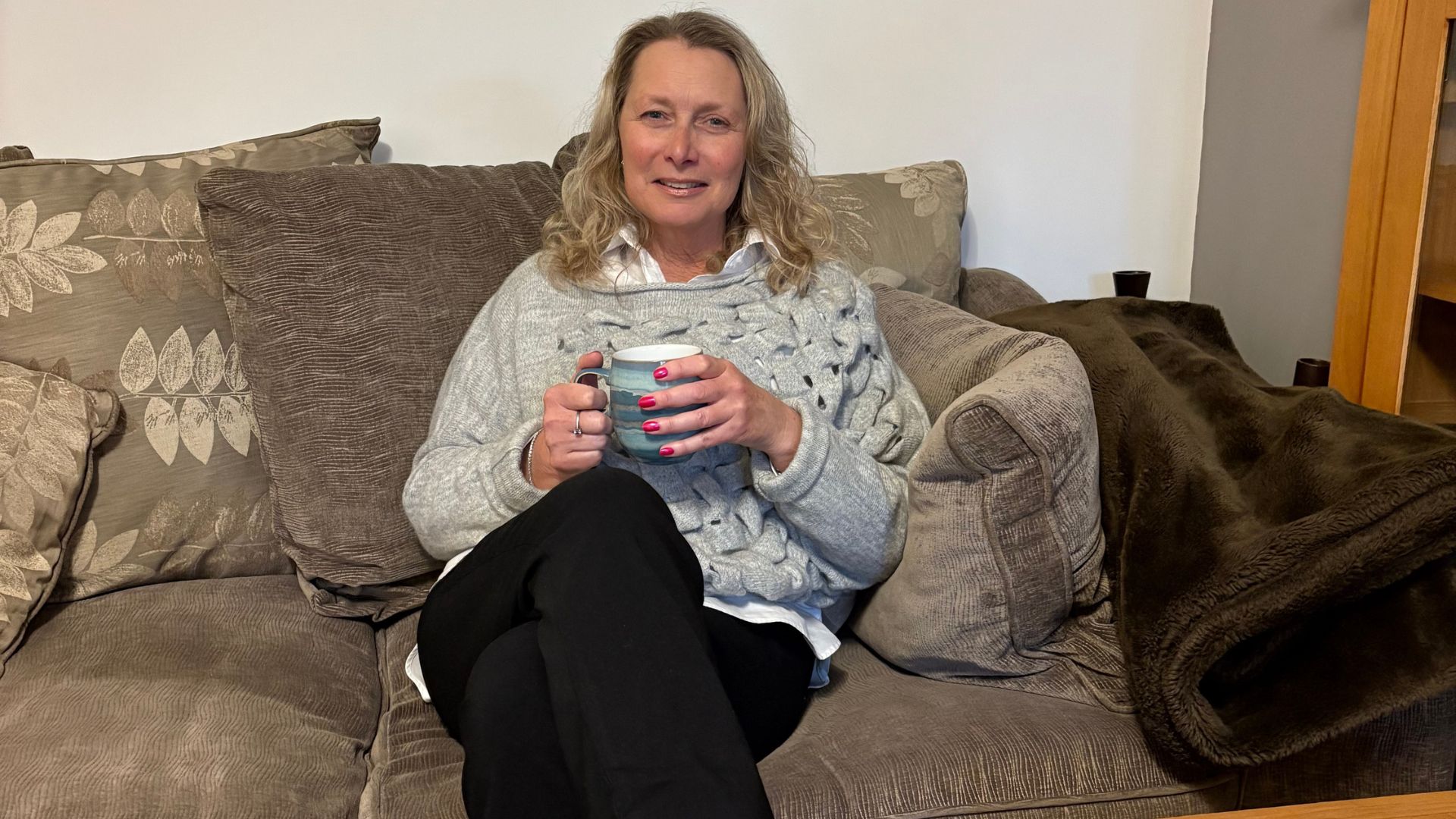 Karen Karen Baker, the hypnotherapist, on her sofa drinking a hot drink, showing how approachable she is.