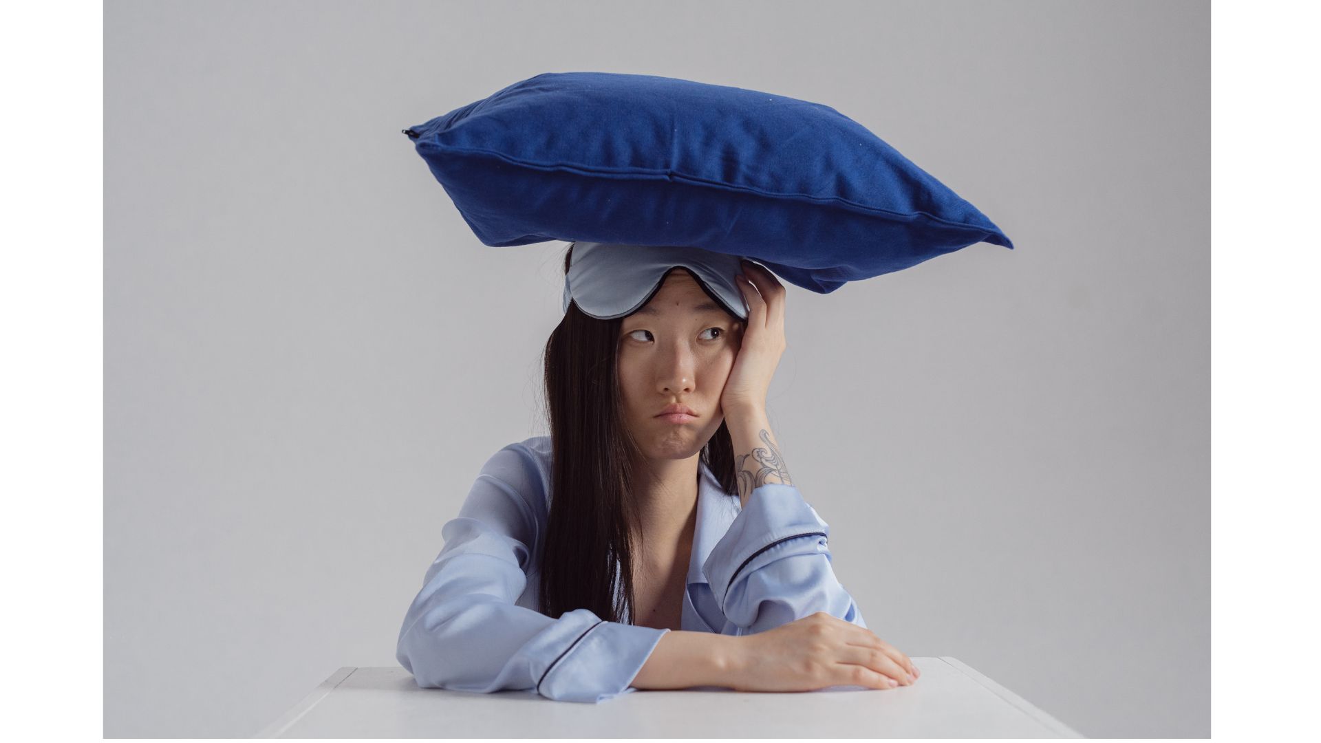 Pillow on Head A picture of a woman in pjs, looking fed up, showing that hypnotherapy can help you sleep better.