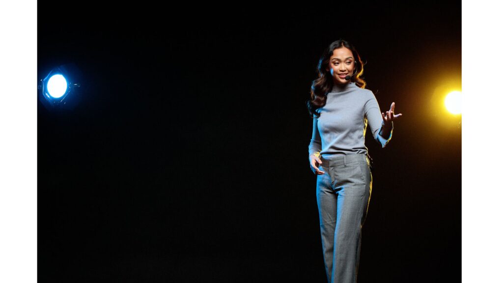 Picture of a woman on stage, with a microphone, showing hypnotherapy can improve confidence when speaking in public.