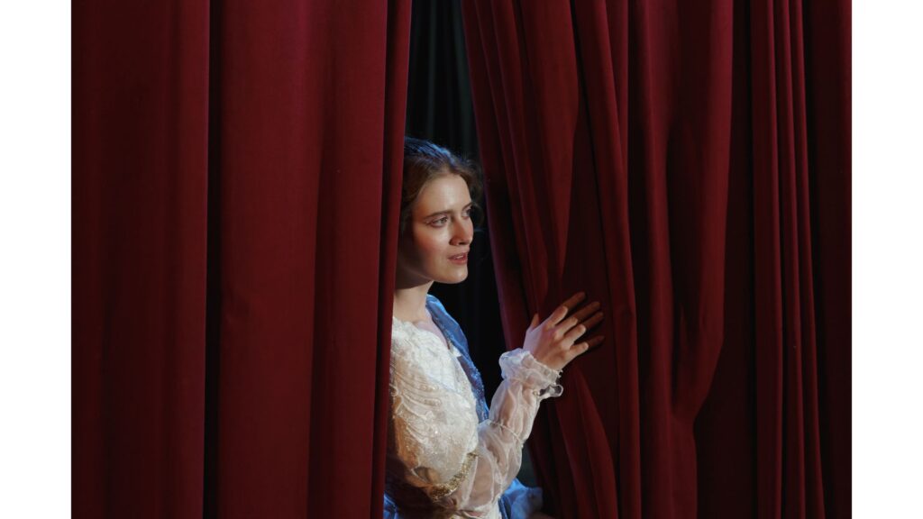 A picture of an actress peaking through some stage curtains, showing that hypnotherapy can help with fear of freezing on stage.
