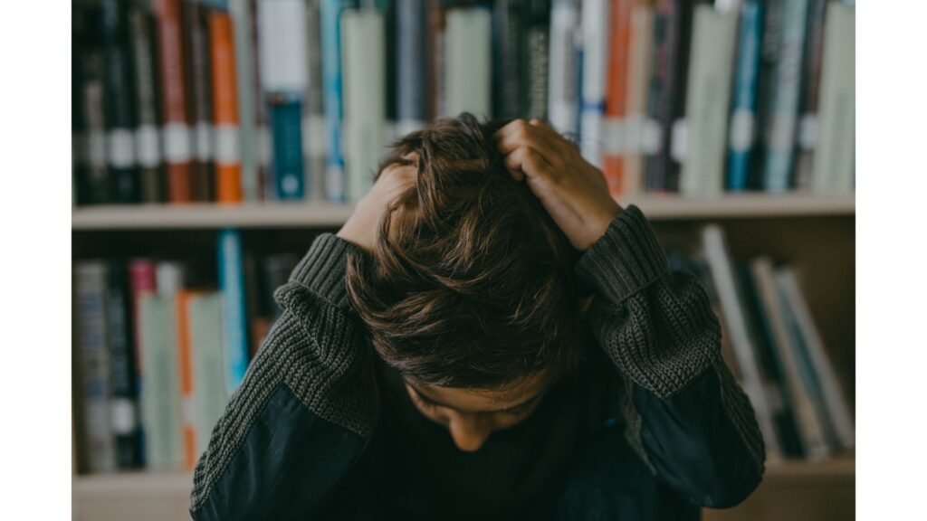 Picture of a man with his head in his hands, pulling at his hair, showing that hypnotherapy could help you stop hair pulling.