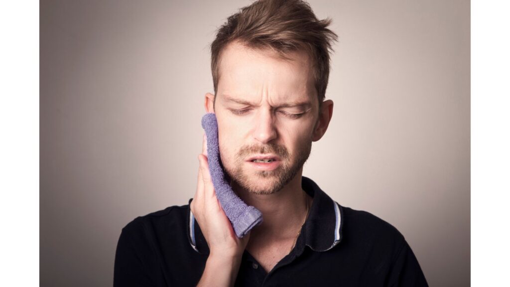 Picture of a man holding a damp cloth to his face, showing that hypnotherapy may help you stop grinding your teeth.